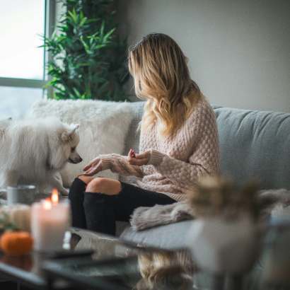 Woman sitting on a couch in a bright home, wearing a thick knit sweater